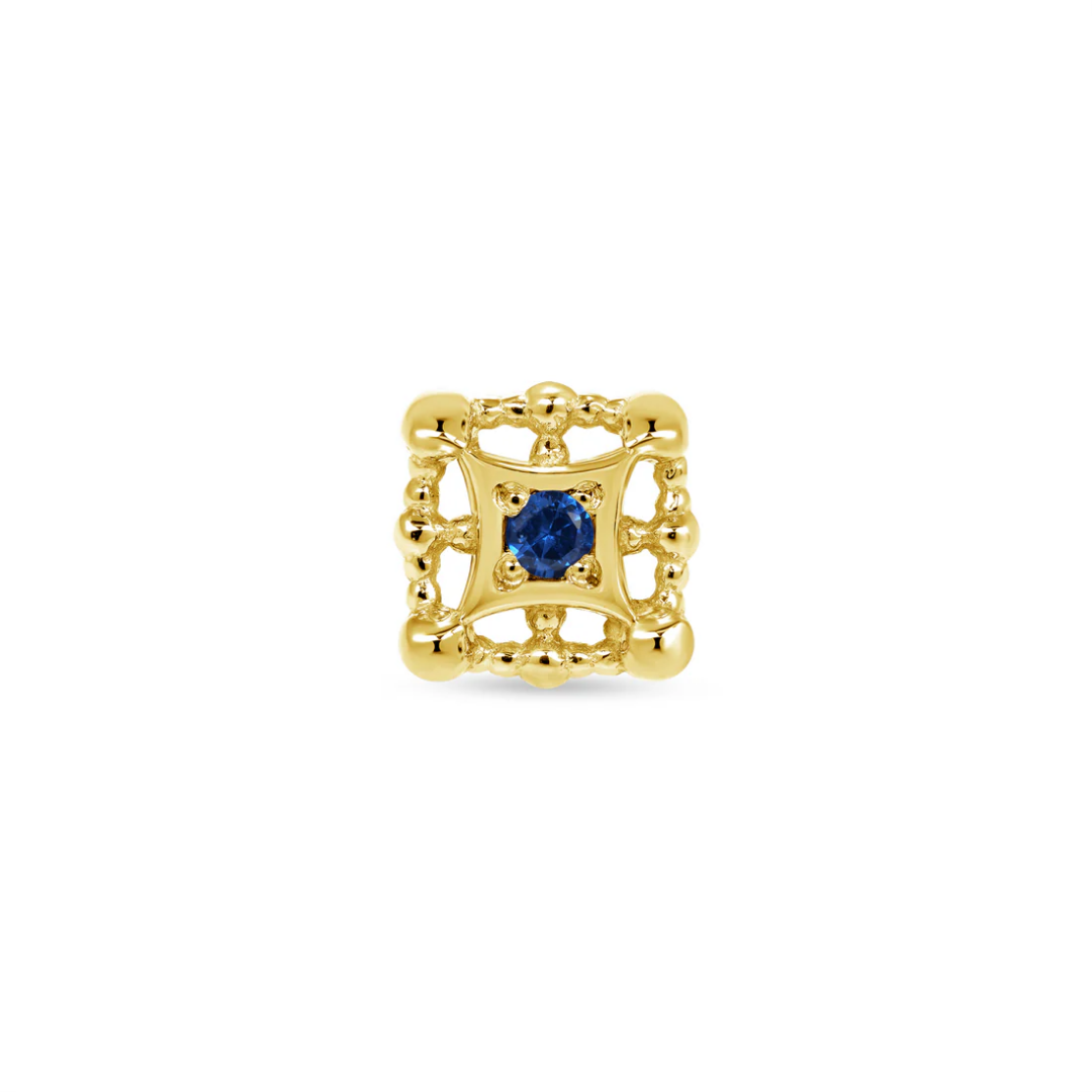 Close-up of a Norvoch gold square piercing end with ornate beaded detailing and a deep blue gemstone set at the centre