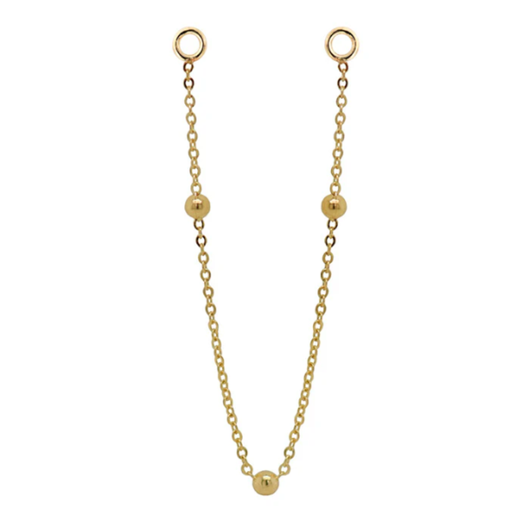 Quetzalli Chime chain crafted from solid 14k gold, featuring a fine link design adorned with three evenly spaced polished gold beads. The elegant connector chain drapes gracefully between piercings, adding soft movement and a refined golden glow.
