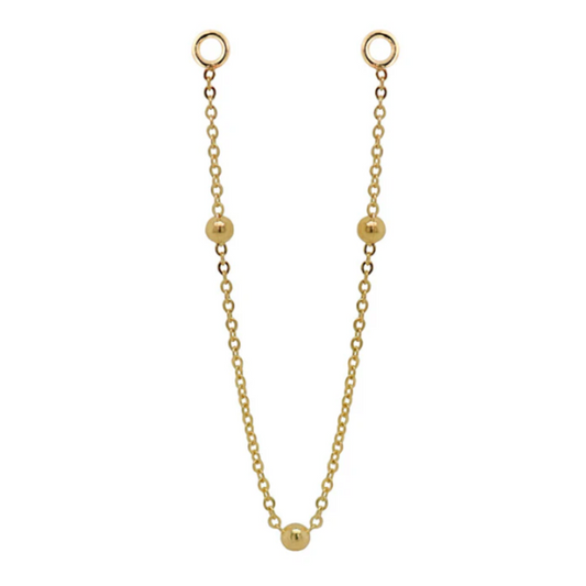 Quetzalli Chime chain crafted from solid 14k gold, featuring a fine link design adorned with three evenly spaced polished gold beads. The elegant connector chain drapes gracefully between piercings, adding soft movement and a refined golden glow.